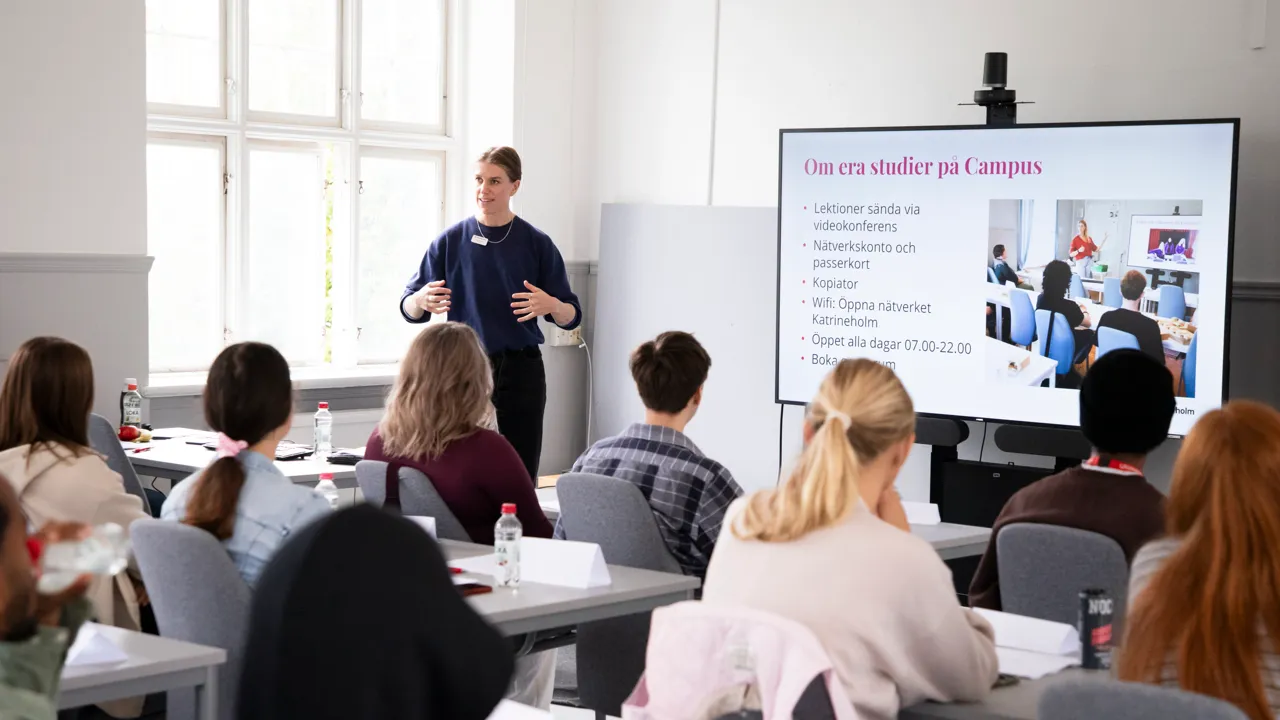 Unga vuxna studenter som sitter i ett ljust klassrum i vita och ljusgrå toner.